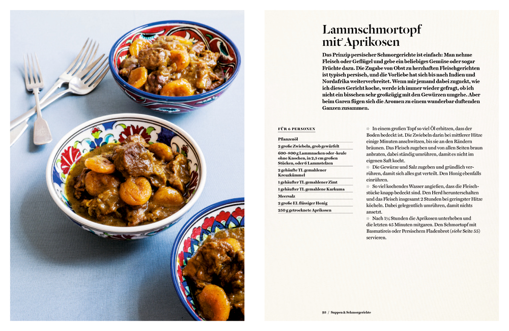 Drei bunte Schalen mit Lammragout und Aprikosen stehen auf einem weißen Tisch neben zwei Silber-Gabeln.