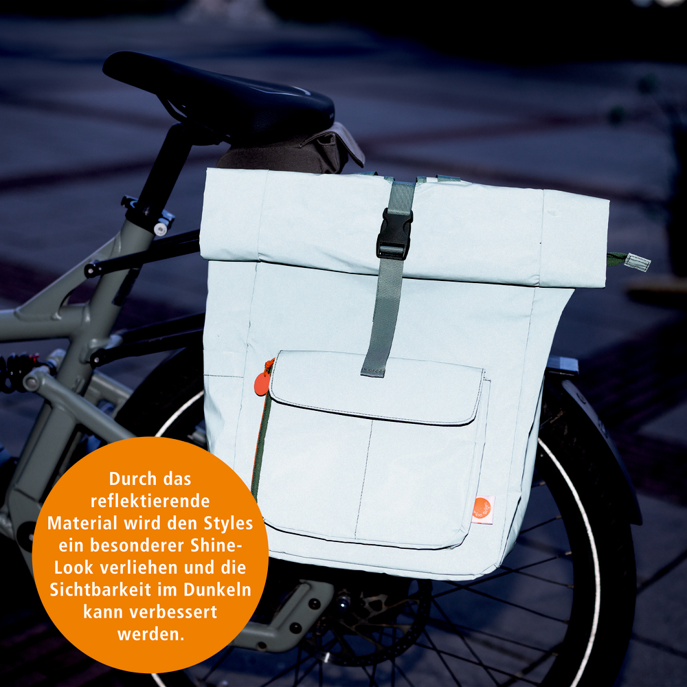 Helle Fahrradtasche mit reflektierendem Material, großer Fronttasche und Steckverschluss am Gepäckträger eines Fahrrads befestigt.