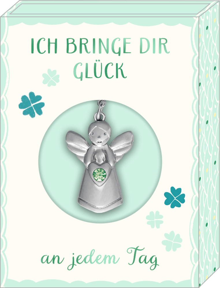 Silberfarbener Engelanhänger mit grünem Stein in herzförmiger Fassung vor Verpackung mit Kleeblattmotiven.
