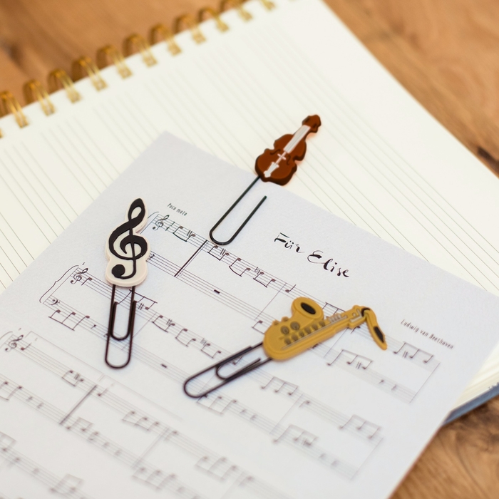 Ein Notenblatt liegt auf einem Noten Notizbuch. An das einzelne Notenblatt sind drei Büroklammern mit Musik-Motiven geheftet